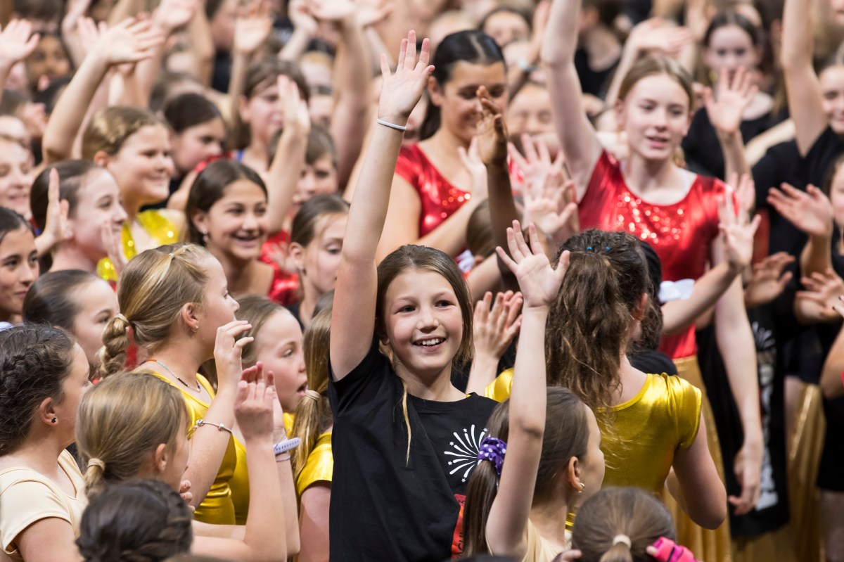 Girl with raised hand amid a crowd of other students at the NSW Schools Spectacular first combined rehearsal 2023