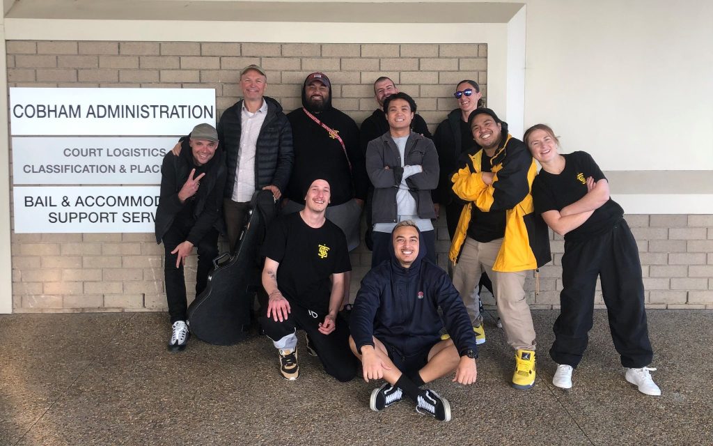 Music. Image is of a group of people mostly dressed in black looking at the camera and smiling.