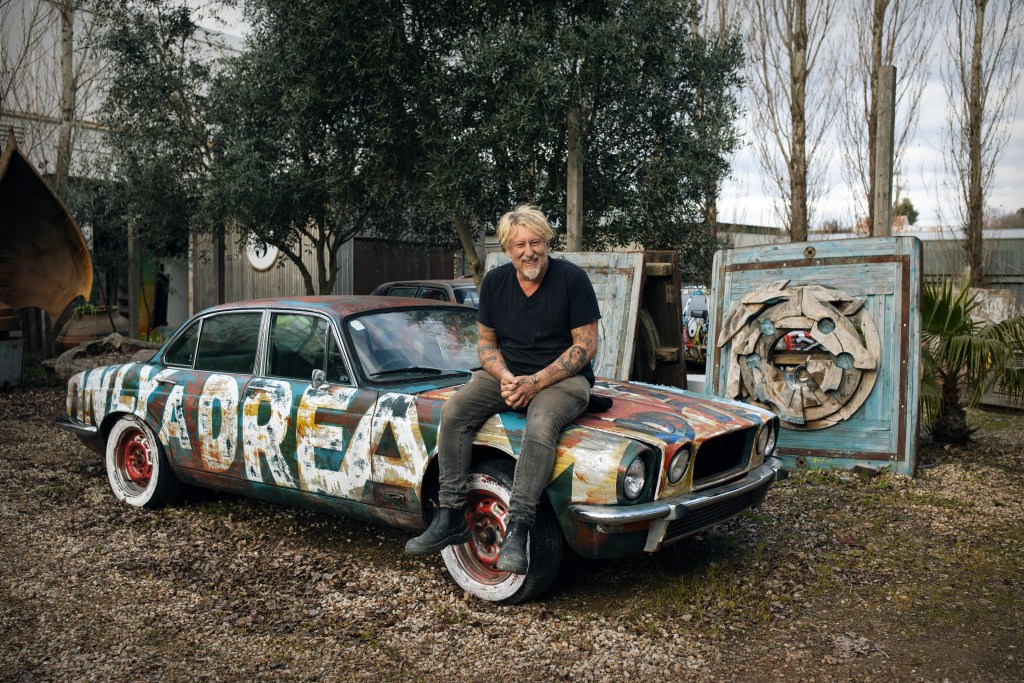 Bromley. Image Is A Man In A Black T-Shirt Sitting On An Old Car Covered In Art/Graffit.