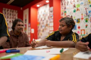 Aboriginal artist Vincent Namatjira sitting with a young Aboriginal student in an art class.