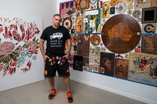 Professional development. Image is a man in shorts and T shit with hands in pockets, standing in front of a wall of artworks.