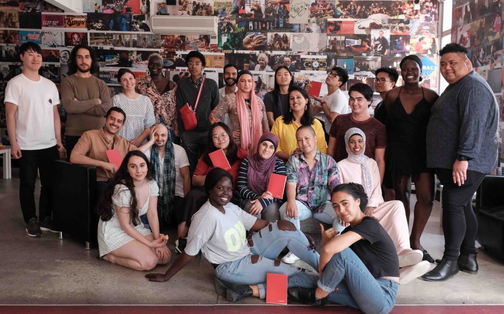 CALD. Image is of a large group of people some standing, some sitting on the ground, from Sweatshop, a Western Sydney-based literary movement.