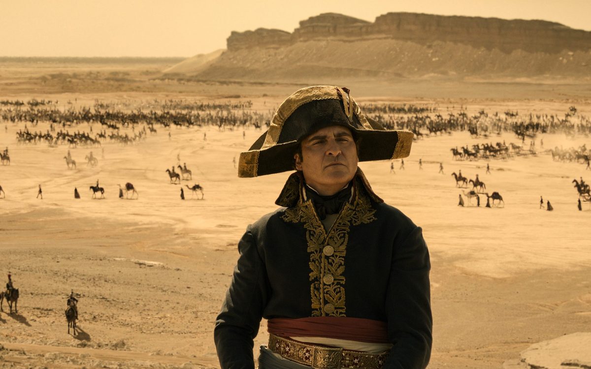 Napoleon. Image is an 18th century French general with three-cornered hat and blue tunic with tiny figures in the background and a desert setting.