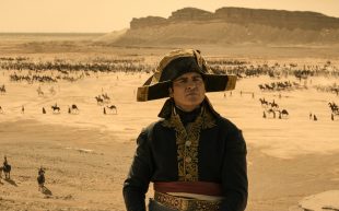 Napoleon. Image is an 18th century French general with three-cornered hat and blue tunic with tiny figures in the background and a desert setting.