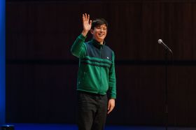 Phil Wang. A young man in a green and blue top is waving.