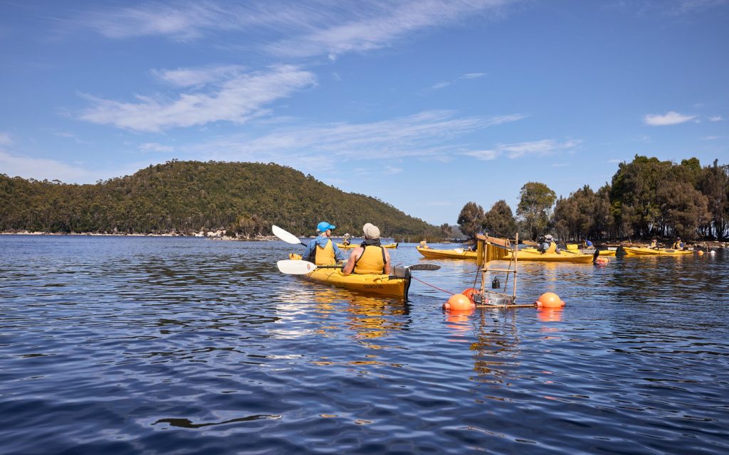 The Unconformity. Image is of performance participants sitting in kayaks on a lake.