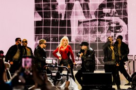 Aguilera. Image is blonde singer in red on stage surrounded by a band dressed in black.