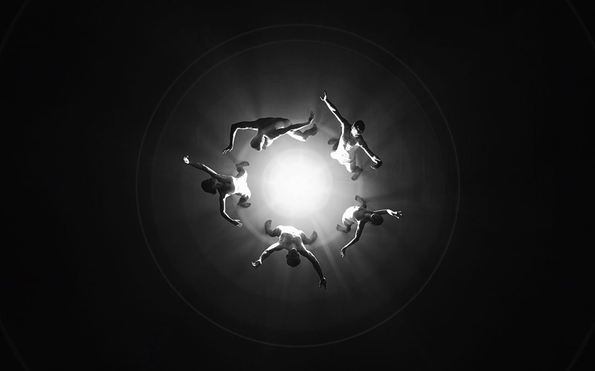 BlakDance. Black and white photo featuring five dancers in various movements in a circle with a spotlight shined on them. The photo is taken from bird’s eye view. Dance.
