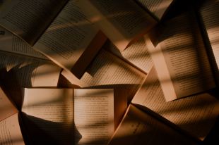 Patrick. Image is of a table filled with open books covered in shadows and strips of light.