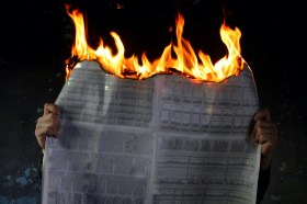 Arts news. Person holding burning newspaper against dark background