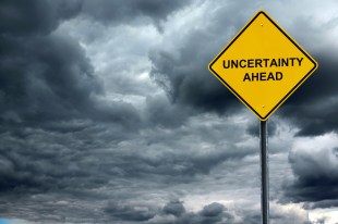 National. Image is grey stormy skies and a yellow diamond shaped road sign saying UNCERTAINTY AHEAD.