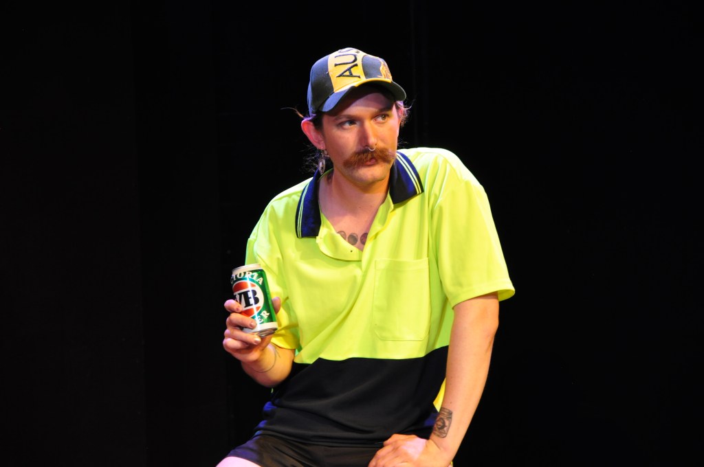 Everything but the kitchen sink. Image is a woman in drag as an Aussie tradie, in high vis shirt, baseball cap, with a fake moustache and can of VB beer.