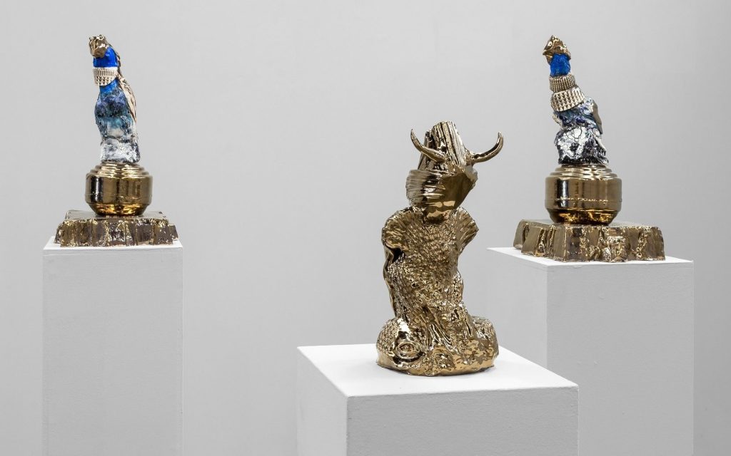 'ARA DOLATIAN: Heavenly Bodies' installation view at James Makin Gallery. Photo: Ivana Smiljanic. Three small sculptures on plinths inside a white gallery space. Each sculpture is gold and blue with towering shapes.