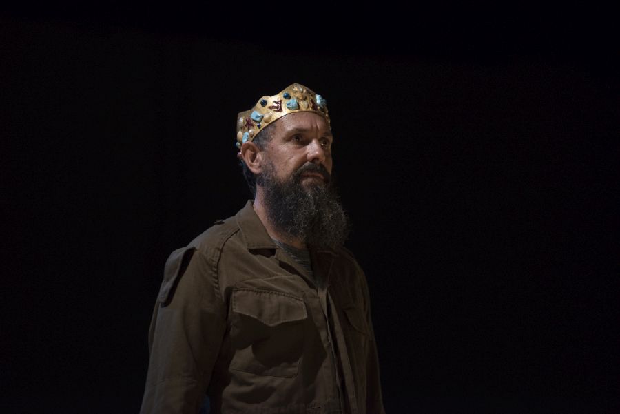 Yirra Yaakin Theatre Company. A bearded man wearing a gold crown on stage sgainst a black background.