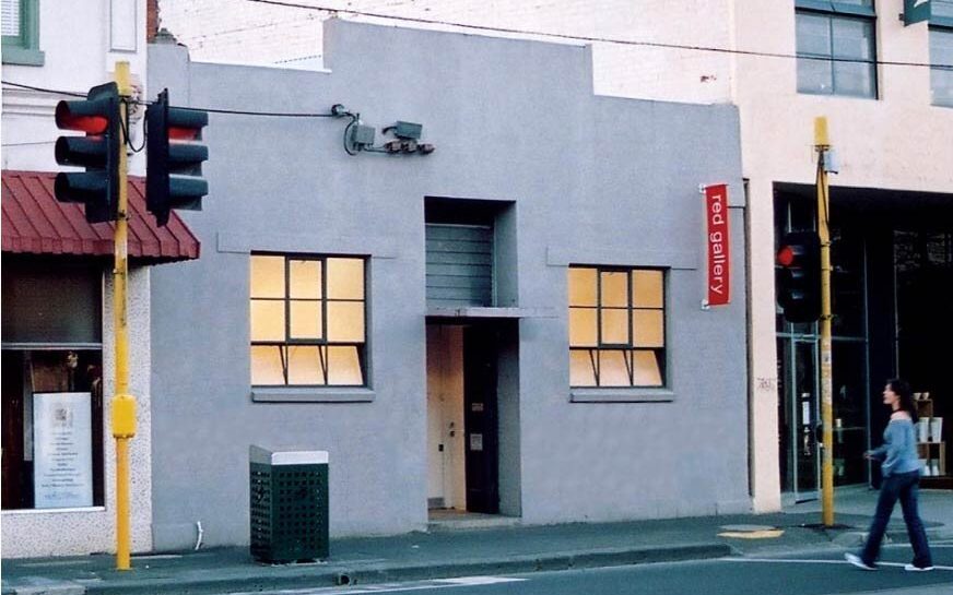RED Gallery. Image is a grey building facade with two windows either side of a middle door.