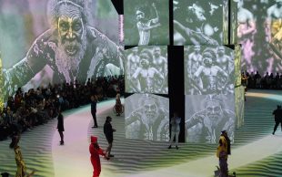 ganbu marra runway. Image is huge immersive space with Indigenous imagery and small figures parading their fashions on the floor.