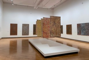 Emily Kam Kngwarry. Image is a gallery with batiks and large paintings hanging from the ceiling and on the walls.