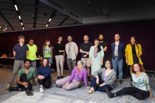 Testing Grounds. A group of artists stand and sit in an arc posing for the photograph.