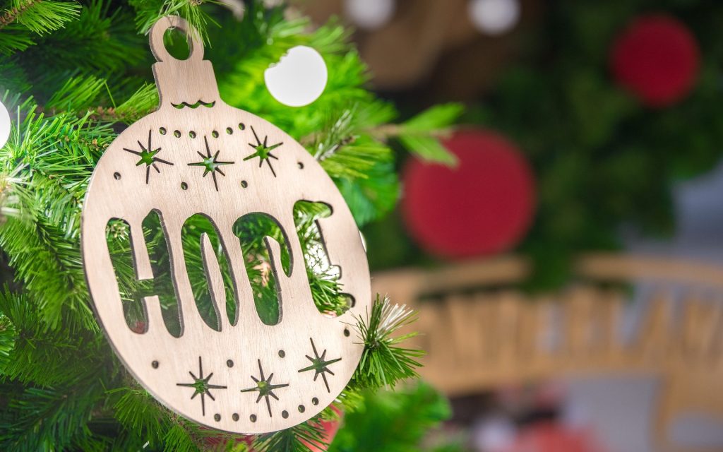 Photo: Arisa Chattasa via Unsplash. Photo of a bauble made out of wood with the word ‘HOPE’ engrained on it, hanging from a Christmas tree.