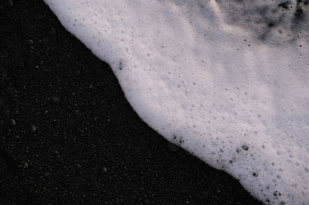 arts appointments. White sea-foam laps on a black sand beach.