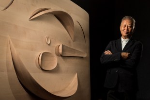 Khai Liew. Asian man standing in darkened room with timber sculpture.