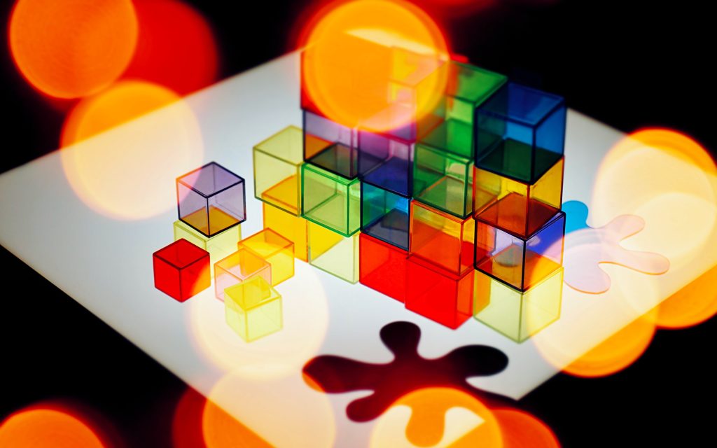 Check out the breadth of ideas and topics covered by Amplify Collective writers. Photo: Mike Bird. Colourful plastic cubes are arranged on a table with round colours of light in the foreground.