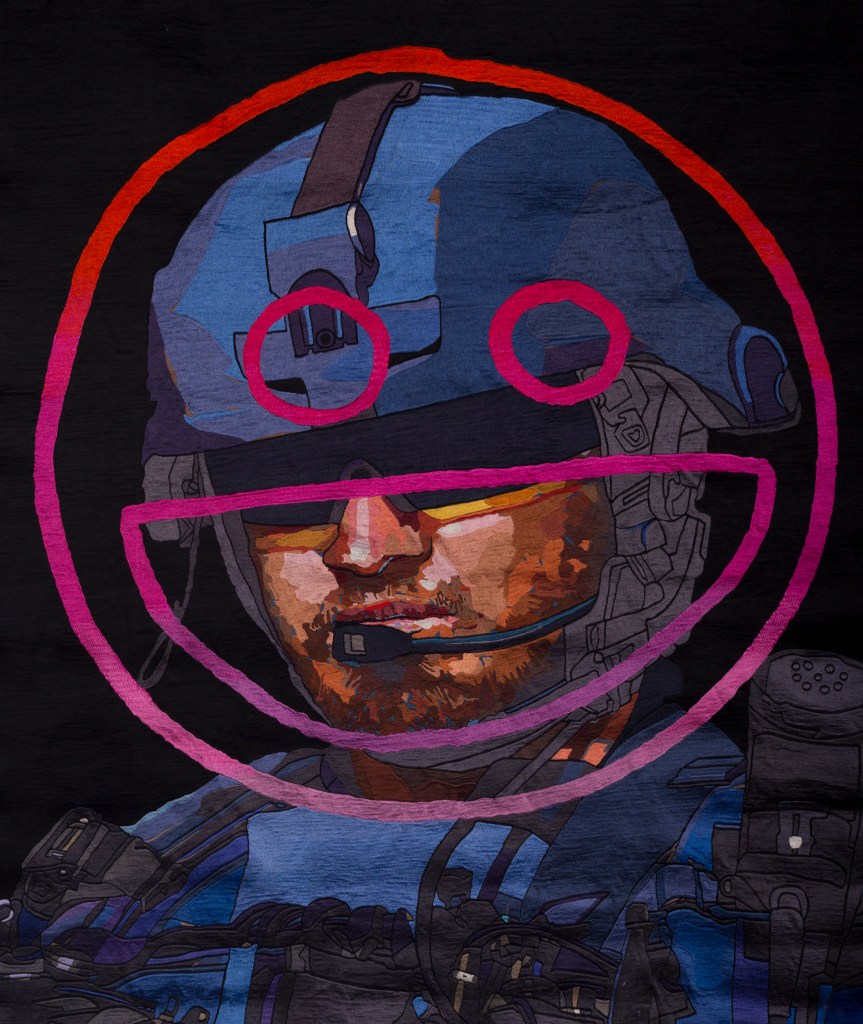 One of Abdul Abdullah’s two works in ‘Violent Salt’. 'All Let Us Rejoice', 2017 is a manual embroidery made with the assistance of DGTMB Studios. Image: Courtesy of Abdul Abdullah and DGTMB Studios. An embroidered portrait of a man wearing heavy armoury gear with a smiley face vandalised across his head.
