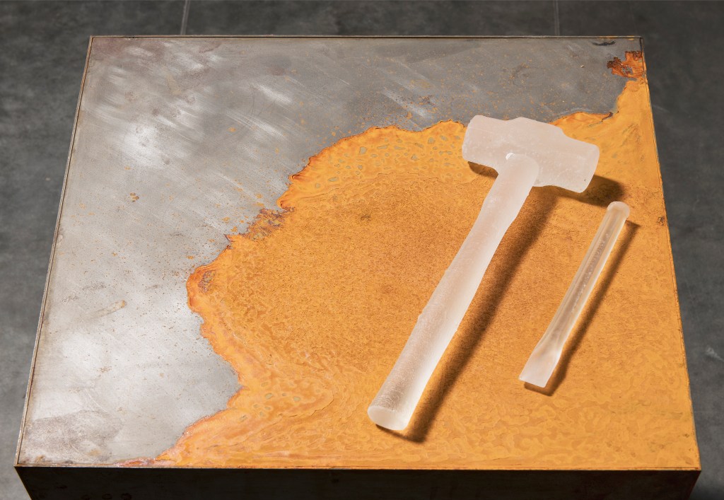 Nicholas Burridge, 'stone artefact' series, 2024. Photo: Brenton McGeachie. A hammer and chisel made of glass is placed on a partially rusted metal stand. 