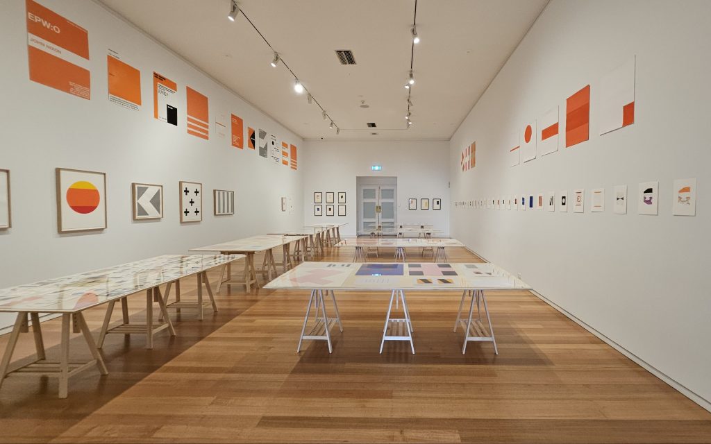 ‘John Nixon—Four Decades, Five Hundred Prints’ installation view at Geelong Gallery. Photo: ArtsHub. Exhibition space with white wall and timber floor, filled with prints and works on paper displayed on wooden tables.