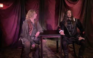 ‘Ruff Trade’. Photo: Steven Dawson. Two performers in 16th century attire sitting on each side of a wooden table. One is looking toward the other, trying to make conversation.