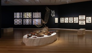 NETS. Image is a display of First Nations artworks and artefacts in a black walled gallery.