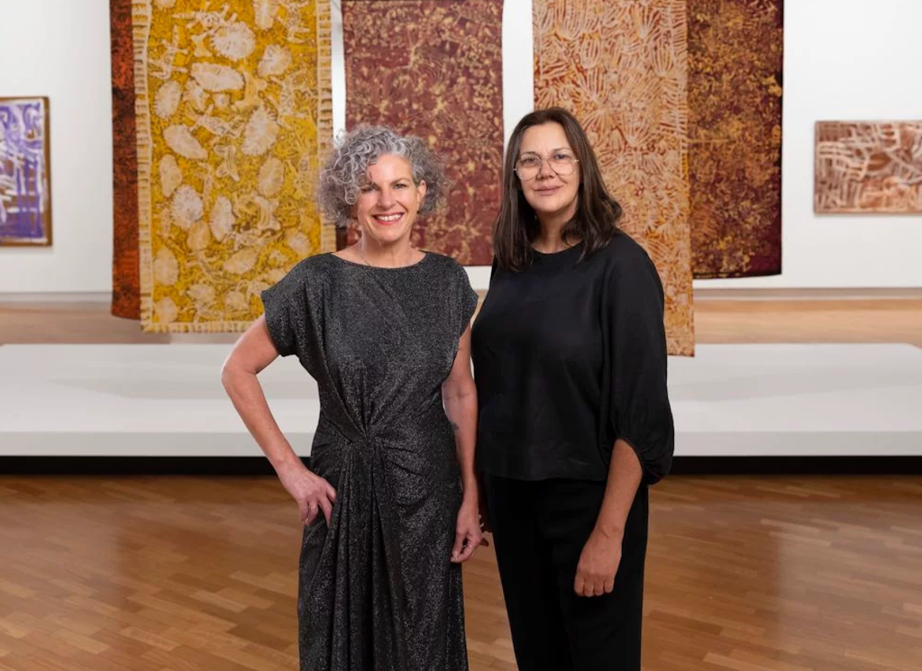 NVAEC, Two women in black stand side by side in front of Indigenous wall hanging art. Kelli Cole, Warumungu and Luritja peoples, Curator, Special Projects, Aboriginal and Torres Strait Islander Art and Hetti Perkins, Arrernte and Kalkadoon peoples, co-Curator, in Emily Kam Kngwarray, National Gallery of Australia, Kamberri/Canberra, 2023. Photo: Sam Cooper.