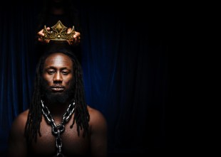 Publicity image for Future D. Fidel's 'La Belle Epoque' at Theatre Works. Photo: Morgan Roberts. A black man is seen emerging from the shadows with a large chain necklace and what appears to be a floating crown above his head.