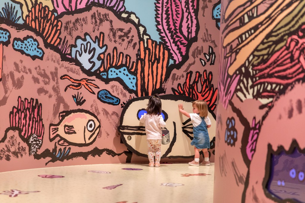 Young kids standing at colourful wall mural by Jean Jullien at NGV International summer festival for kids.