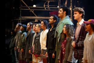 RENT: The Musical. Image is a diagonal shot of a line-up on stage of young men and women looking off to the left and singing.