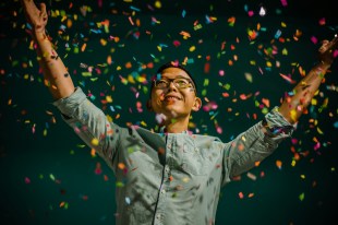 Person with arms raising and smiling and colour confetti showing down. Art Prize