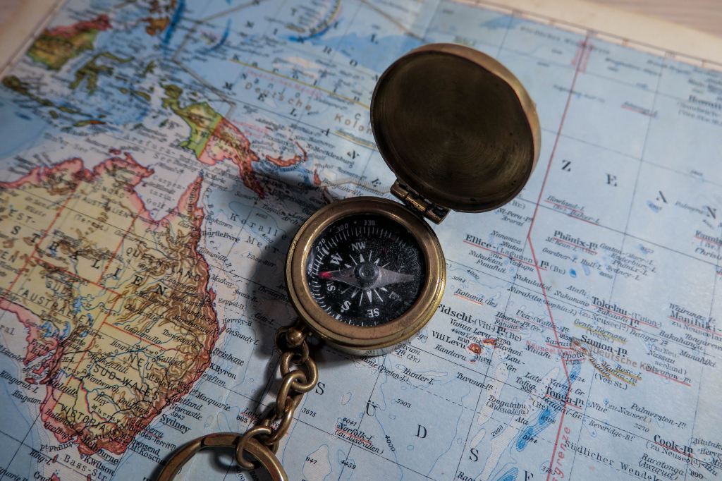 A photograph of an old-fashioned brass compass sitting next to a map of Australia and the South Pacific.