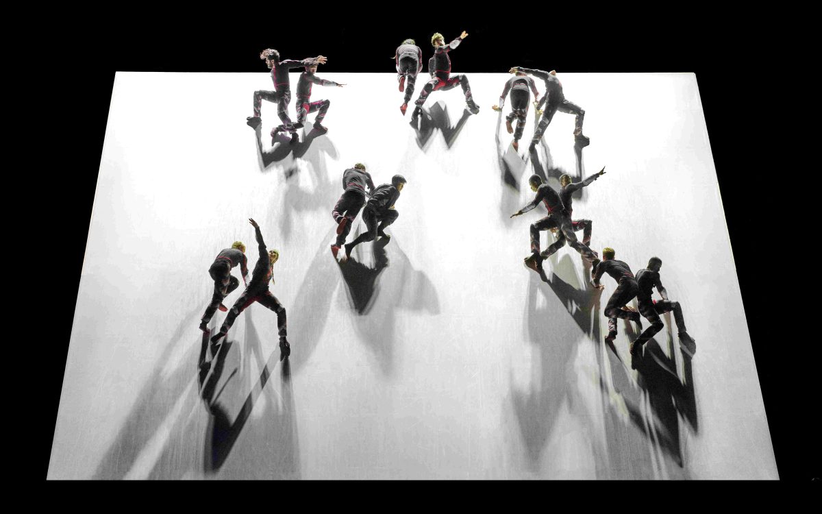 ‘Skid’ by Damien Jalet for GöteborgsOperans Danskompani. Photo: Lennart Sjoberg. Dancers battling gravity on a tilted white stage. They are upright with knees bent and arms in different movements.