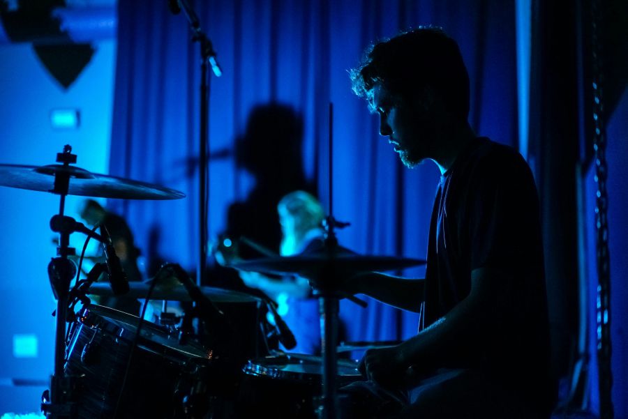 live music: a male musician playing the drums in darkened bright blue light on a small stage.