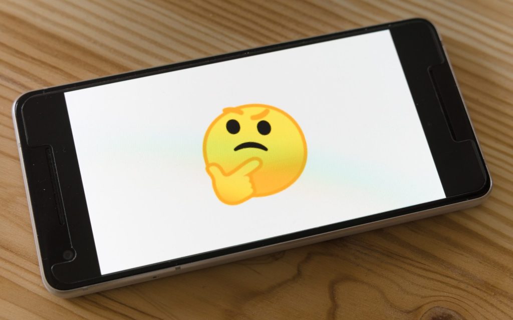 Photo of a cellphone on the table with a questioning emoji displayed on the screen against a white background.