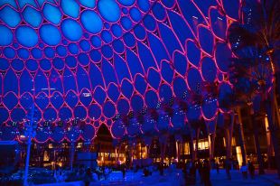 A dome like architectural structure with blue and neon pink lights projected throughout at night.