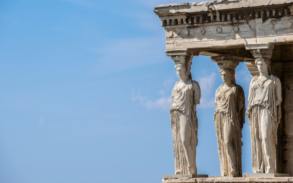 Photo: Stelios Kazazis, Unsplash. Three sculptures of goddesses on the architectural column of the Parthenon.