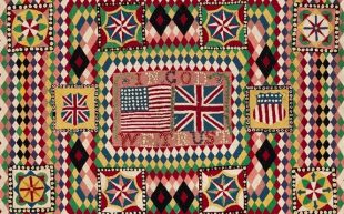Quilt work from the exhibition 'Quilts: The Fabric of War 1760-1900' at The David Roche Collection. Photo: Supplied. A harlequin quilt pattern with red, pink, yellow, blue green, white, purple and black diamond patches. It features various emblems, the US flag, the union jack and the words 'IN GOD WE TRUST'