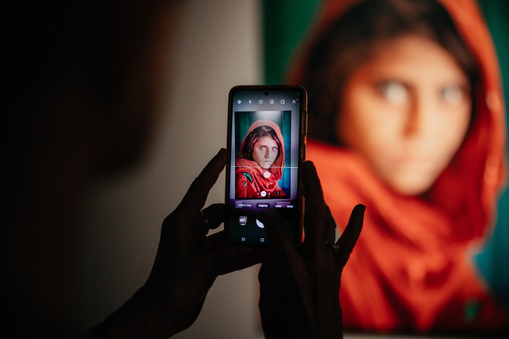 A phone camera is held up to a photo of Steve McCurry's famous 'Sharbat Gula' (Afghan Girl) photo