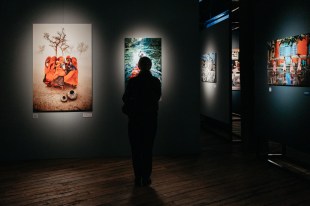 ICONS. installation view of a black walled gallery with large colourful photographs hanging on the walls.