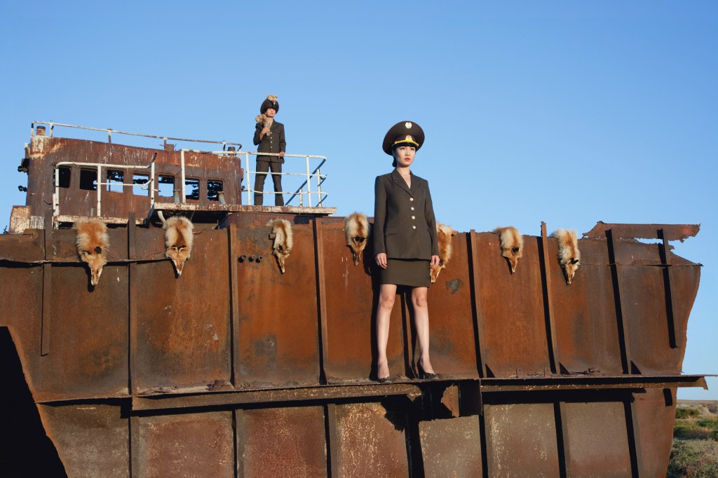 Almagul Menlibayeva, 'Transoxiana Dreams', 2011, video still. Image: Supplied. Two figures wearing a fitting army green suit stand on a rusted shipwreck with fox skin hanging over the edge. 
