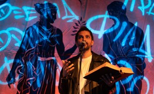 Greek-Australian poet and spoken word performer Luka Lesson gestures with his right hand while holding a book in his left.