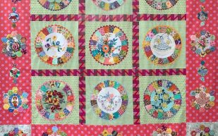 ‘Tutti Fruiti’ by AQC tutor Chris Jurd, part of the AQC Teach Me display. Photo: Supplied. An intricate quilt with a pink dotted background and floral motif, nine squares lined up in the centre, each with a round patterned floral motif.