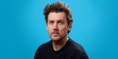 Profile photo of a man with brown hair and a black t-shirt against a blue background. Daniel Connell.