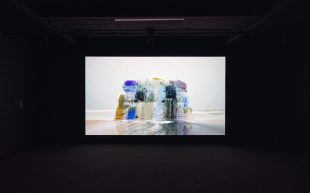 Installation view, 'Dawn Ng: Avalanche', Institute of Modern Art, Brisbane, 2024. Image: Courtesy of the artist and Sullivan+Strumpf. Photo: Carl Warner. A video still against a black background that depicts a ice block coloured in different shades and melting.